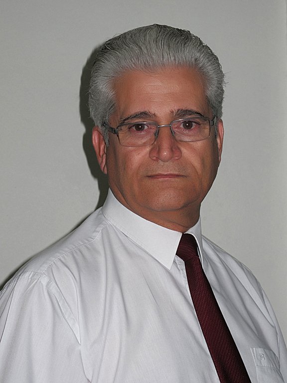 Portrait of Steven Stavri in a white shirt and burgundy tie, wearing glasses.